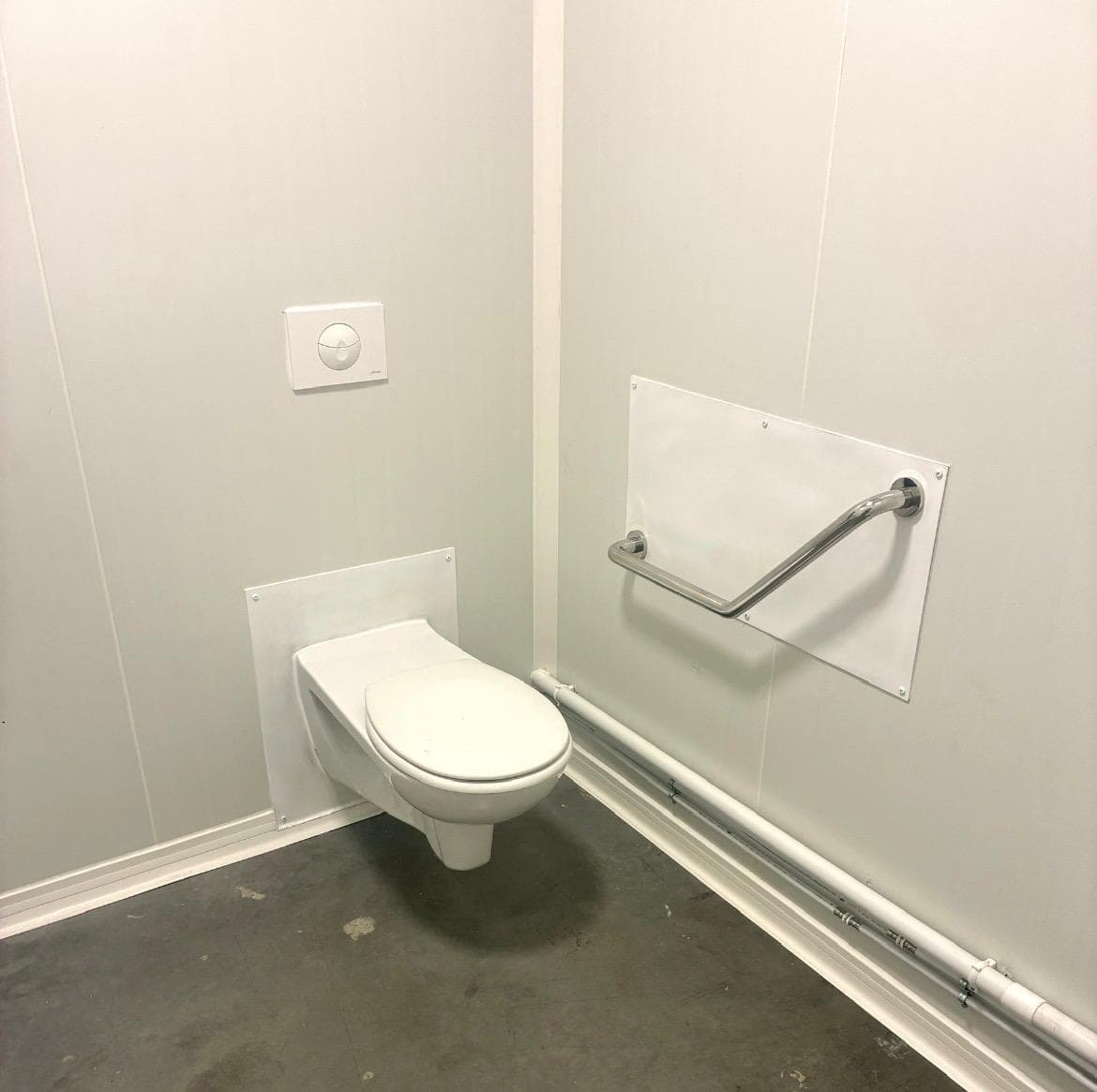 WC suspendu et barre d'appui fixés sur plaques acier dans un local sanitaire